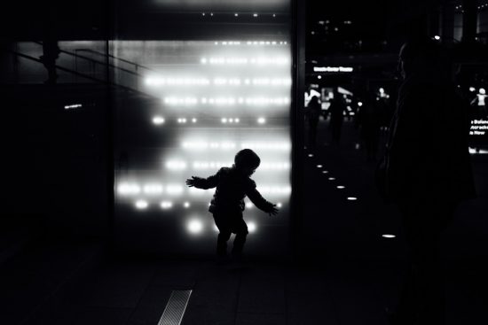 Black and white image of a child in silhouette against a wall with muted white lights.