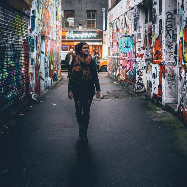 a woman walking down a narrow street lined with bright posters