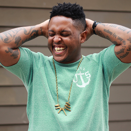 Photo of Danez Smith in a mint green t shirt, smiling with their hands behind their head