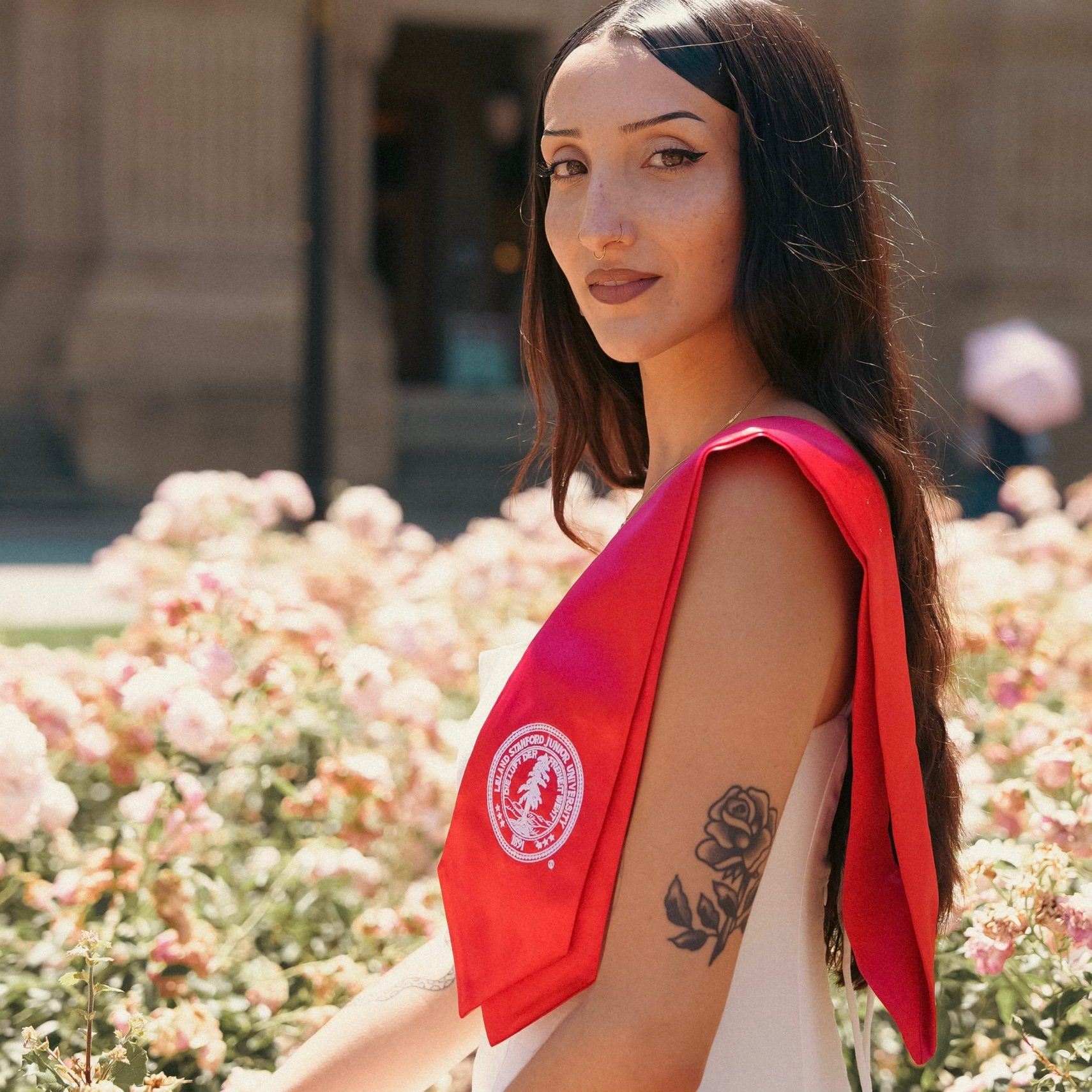 A person with long hair standing in front of Memorial Church wearing a Stanford honor stole