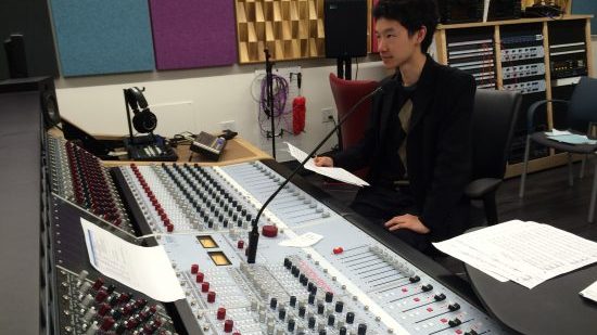 Person sitting at an audio recording console holding sheet music.